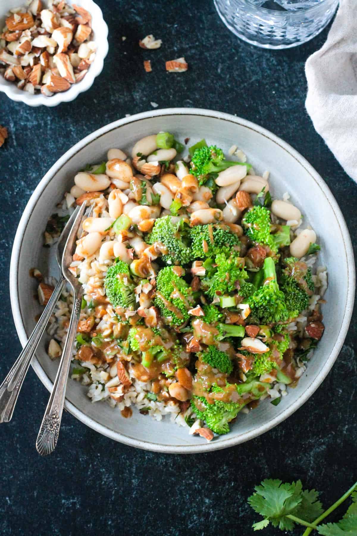 Steamed broccoli, brown rice, white beans, and almonds in a flat bowl.