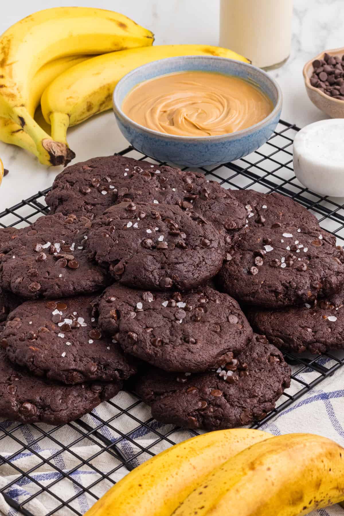 Pile of cookies sprinkled with flaky sea salt on a cooling rack.