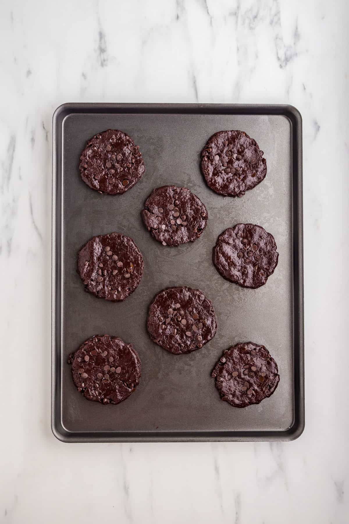 Raw dough shaped into round cookies on a baking sheet.